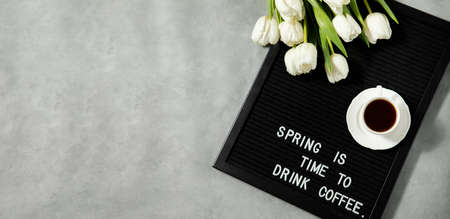 Cup of coffee and white tulips on a felt board with the inscription in English spring.の写真素材