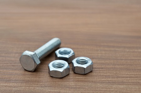 Metal fasteners, bolt and nuts for construction, close-up on a wooden background. Selective focus.の写真素材