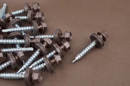 Metal fasteners. Several tapping screws for mounting metal roof, close-up on a brown background. Selective focus.の写真素材