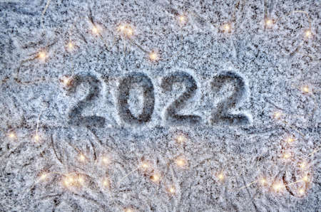 Inscription 2022 on a snow-covered surface with christmas lights.の写真素材