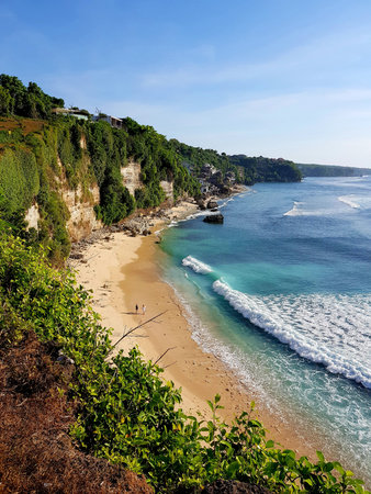 Ocean coast, clean, beautiful, summer beach with light waves. Two, a man and a woman, are walking...