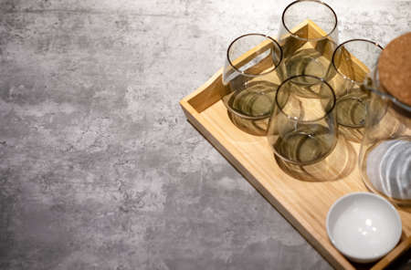 Glass mugs and a jug sit on a gray tabletop on a light, wooden tray.の写真素材