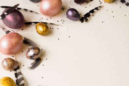 Easter holiday. Beautiful, multi-colored, mother-of-pearl eggs lie on a uniform beige background. Feathers all around.の写真素材