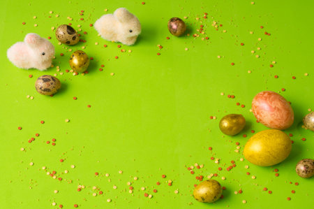 Easter holiday. Beautiful, nacreous eggs on a green background. Two little rabbits are sitting side...