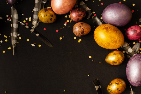 Easter holiday. Multi-colored, mother-of-pearl chicken and quail eggs lie on a black background,...
