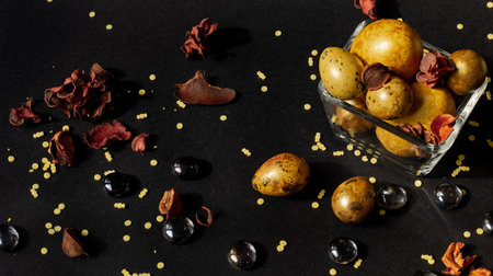 Easter holiday. Beautiful, golden eggs of various sizes lie in a small glass vase on a black...