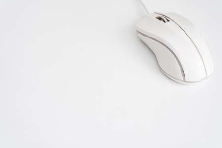 A white computer mouse of an ergonomic shape, located in the upper right corner on a white background of the table.の写真素材