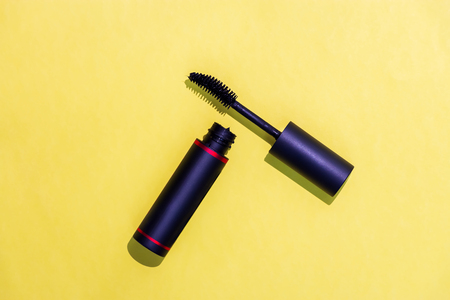Black mascara bottle and curve brush isolated yellow background. Hard light. Concept cosmetic and fashion.の写真素材