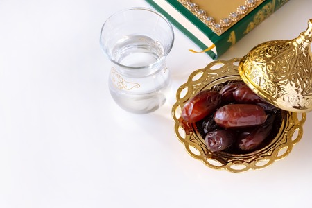 Organic dried dates in traditional arabic golden plate, cup of pure drinking water and quran book. Ramadan concept.の写真素材