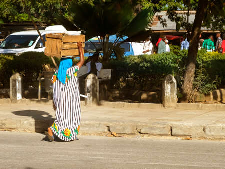 African or Indian woman crosses the road. and carries wooden box on head. Zanzibar, Tanzania, Africa.のeditorial素材