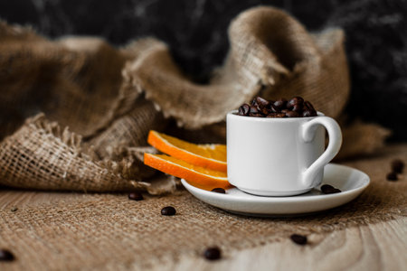 Coffee beans, a white cup on the table. Orange slices. Dark and beige background.の写真素材