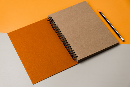 Design concept - top view of spiral notebook and pencil on orange and gray background for mockupの写真素材