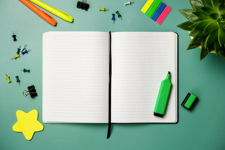 Top view of blank open notebook with stationery on green background.