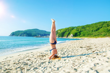 young, beautiful, red-haired girl practices yoga on the beach. headstandの写真素材