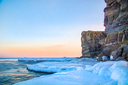 High cliffs into the sea, all in ice. Crag at sunset in the ice. a beautiful landscape from the outgoing Sun. Winterの写真素材