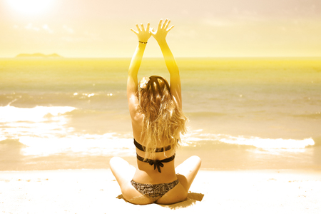 a young, beautiful girl with red hair, in a bikini. practices yoga on the white sand and turquoise sea. harmony with nature.の写真素材