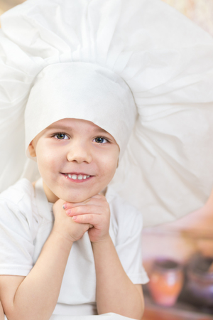 the little boy is preparing cake and pancakes. Dressed like a chef child dough prepares food. wooden house and Pancake weekの写真素材