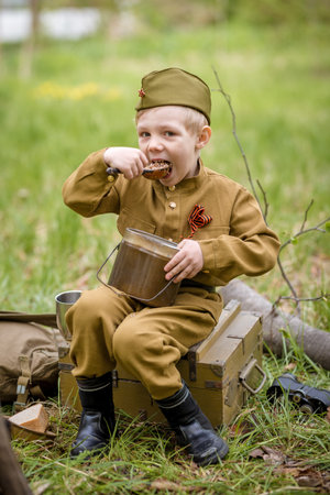 a boy in a military uniform in a clearing, sitting by a campfire with a German shepherd.Two friends...