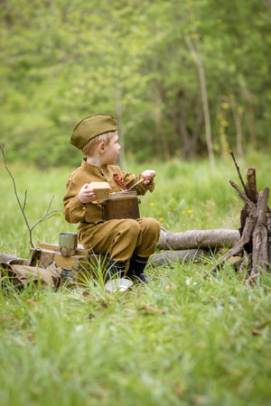 a boy in a military uniform in a clearing, sitting by a campfire with a German shepherd.Two friends defend the motherlandの写真素材