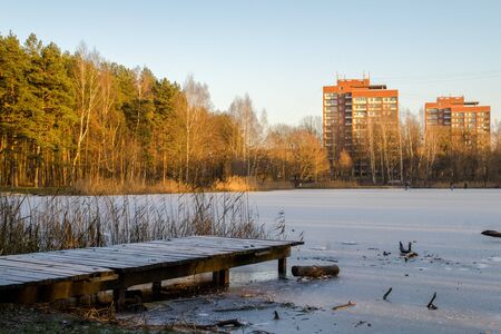 
Morning by the lake in the winter. Lake near forest and with tall brick houses in the background. And the wood bridge in the foreground.の写真素材