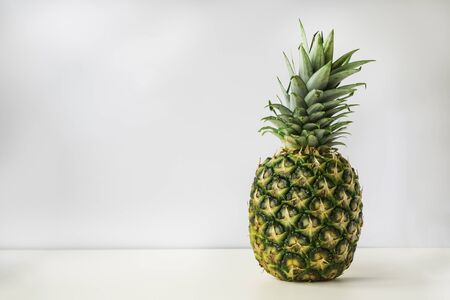 a whole ripe pineapple stands on a white surface with a light gray background.の写真素材