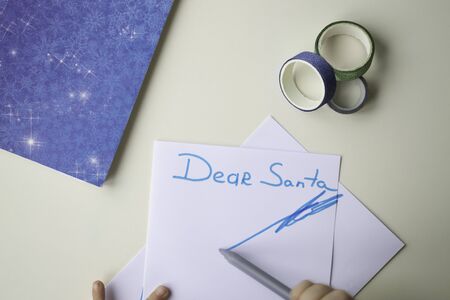 A white sheet of paper, a blue note with snowflakes, a felt-tip pen and a shiny multi-colored decorative scotch tape. Baby hands paint and write letter. The concept of concentration, winter and plans.の写真素材