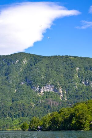 Two hang gliders descend from the mountains. Mountain landscape, lake and mountain range â Lake Bohinj, Slovenia, Alps.の写真素材