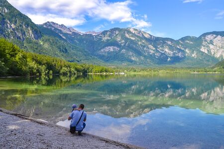 Father and baby admire calm mountain lake on a bright sunny day. Man hugs son on a lake birch, and looks into the distance.の写真素材