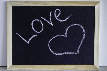 Heart painted with chalk and the inscription Love. Wooden chalkboard with picture. Valentine day and love concept.の写真素材