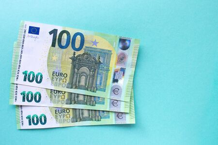Three 100 Euro banknotes on the left side against a blue background. Folded in the form of a fan. The concept of money and finance. With place for text.の写真素材