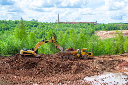 In a quarry with red clay, a yellow excavator with a large bucket.