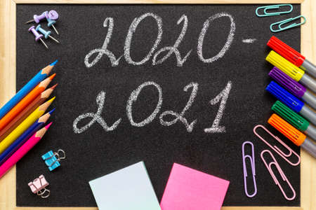 Back to school and new academic year concept. Various stationery: pencils, felt-tip pens, paper clips and stickers. Lettering 2020-2021 on school blackboard.の写真素材