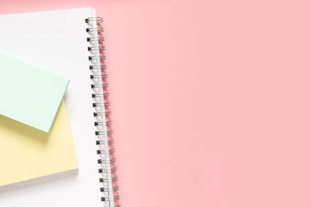 A white notebook with a spiral and two multi-colored stickers on top. Layout and flat lay with place for text on a delicate pink background. Concept back to school.の写真素材