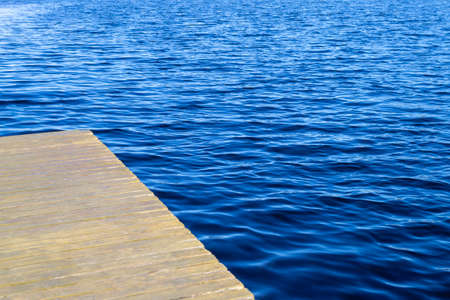 Empty wooden pier and blue water surface with small waves. High angle view to lake, sea or river. Water texture. Copy space, place for text.の写真素材