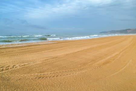 Gava Playa beach in Castelldefels, Barcelona, Spain. Bright seashore cleaned of debris and tire tracks. Big waves, mountains in the background. Morning in natureの写真素材