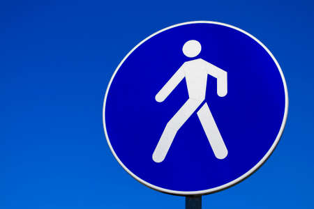 Road sign for pedestrians. Pedestrian zone. Round blue traffic sign with a white man against the sky. With place for text, copy space.の写真素材
