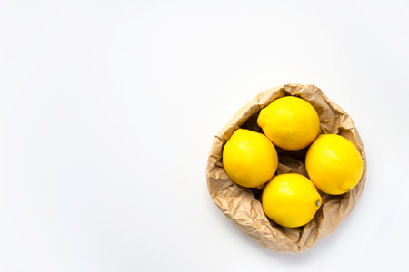 White background and eco packing with lemon. Four ripe lemon on gray background. Group of fresh lemon in recycling paper bag. Place for text, copy spaceの写真素材