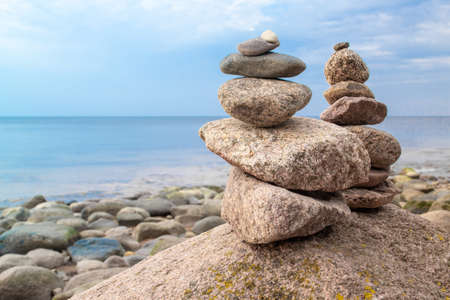 Two stones pyramid on the seashore at sunset. Pebble beach, beautiful view. Rest and seaside vacation. Concept of balanced life, harmony and relax.の写真素材
