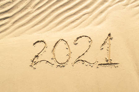 Inscription 2021 on sea or ocean shore. Drawing on wavy sand texture. Top view, copy space. New year and Christmas concept.の写真素材