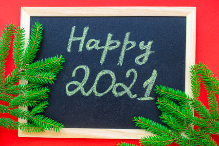 Red background. Chalk handwritten inscription Happy 2021, on a chalkboard. Green branches of Christmas tree in a circle. Flat lay.の写真素材
