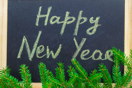 Happy New Year. Handwritten inscription on chalkboard. Green branches of Christmas tree. Flat lay.の写真素材