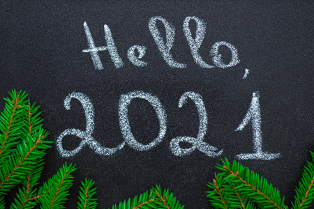 New year concept. Chalk handwritten inscription Hello 2021, on a chalkboard. Frame from green branches of Christmas tree in a circle. Flat lay.の写真素材