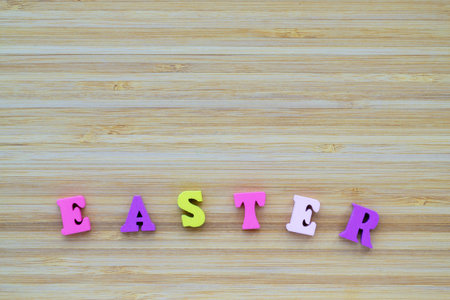 Inscription Easter made from small wooden, multi colored letters. On a striped, textured, wooden...