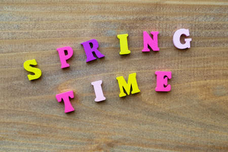 Concept of early spring. Inscription Spring time from small wooden, multicolored letters. On a wooden, textured background.の写真素材