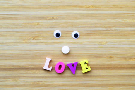 Smile from the inscription love with colored wooden letters and eyes. Minimalism style. Striped, textured, wood background. The concept of love, relationships, Valentines Day.の写真素材