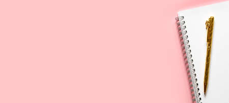 Extra wide banner. Back to school. Golden pen and white notebook with a spiral. Layout and flat lay with place for text on a delicate pink background.の写真素材