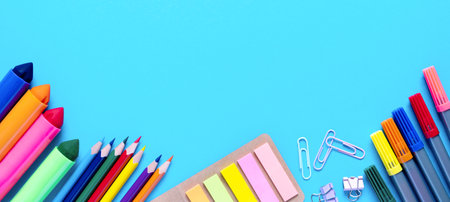 Wide banner. Colorful pencils, felt-tip pens, brushes, stickers and stationery flat lay. School office supplies lie from below on light blue background. Back to school and new academic year concept.の写真素材