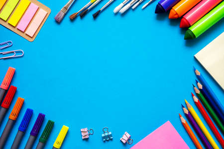 Frame from school office supplies. Colorful pencils, felt-tip pens, brushes, stickers and stationery flat lay on blue background. Back to school concept.の写真素材