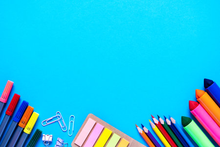 School office supplies lie from below on light blue background. Colorful pencils, felt-tip pens, brushes, stickers and stationery flat lay. Back to school and new academic year concept. Copy spaceの写真素材