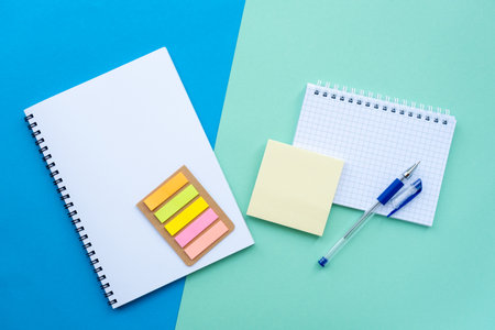 Back to school concept. Top view, above. Flat lay with spiral notepad, notebook, sticker, and office supplies on blue background.の写真素材